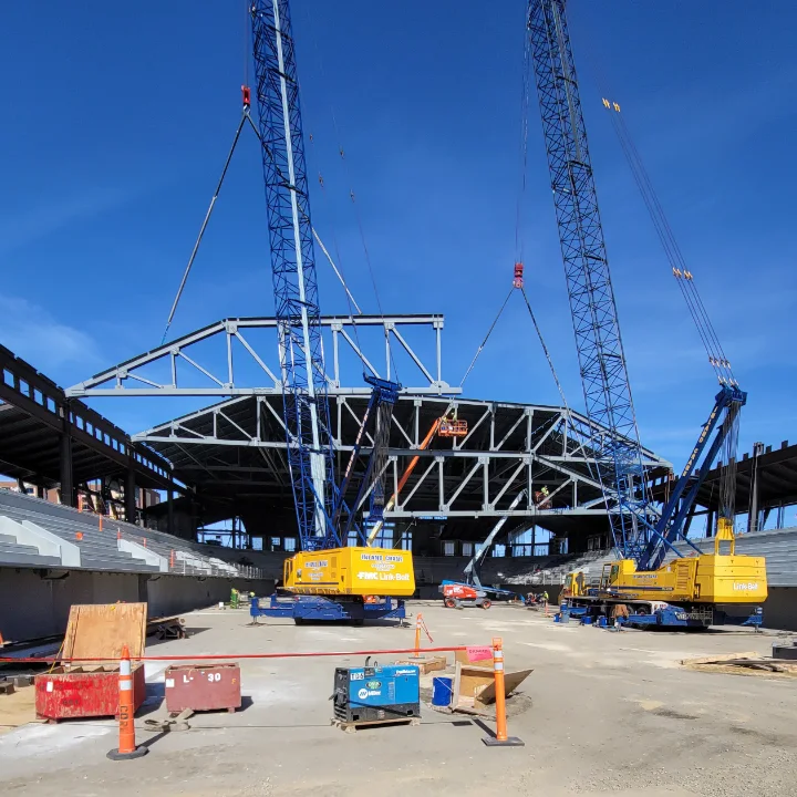Two cranes lifting a steel roof truss into place