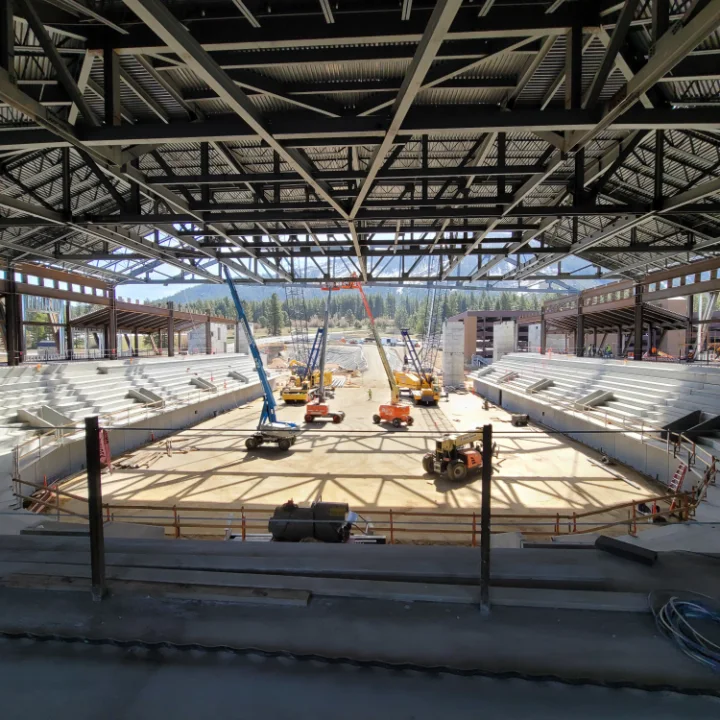 Steel roof structure over an arena under construction, with lifts working on the floor