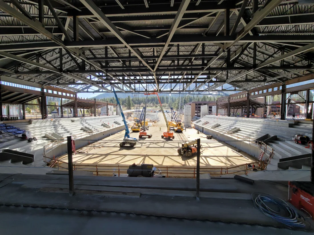 Steel roof structure over an arena under construction, with lifts working on the floor