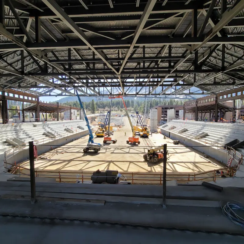 Steel roof structure over an arena under construction, with lifts working on the floor