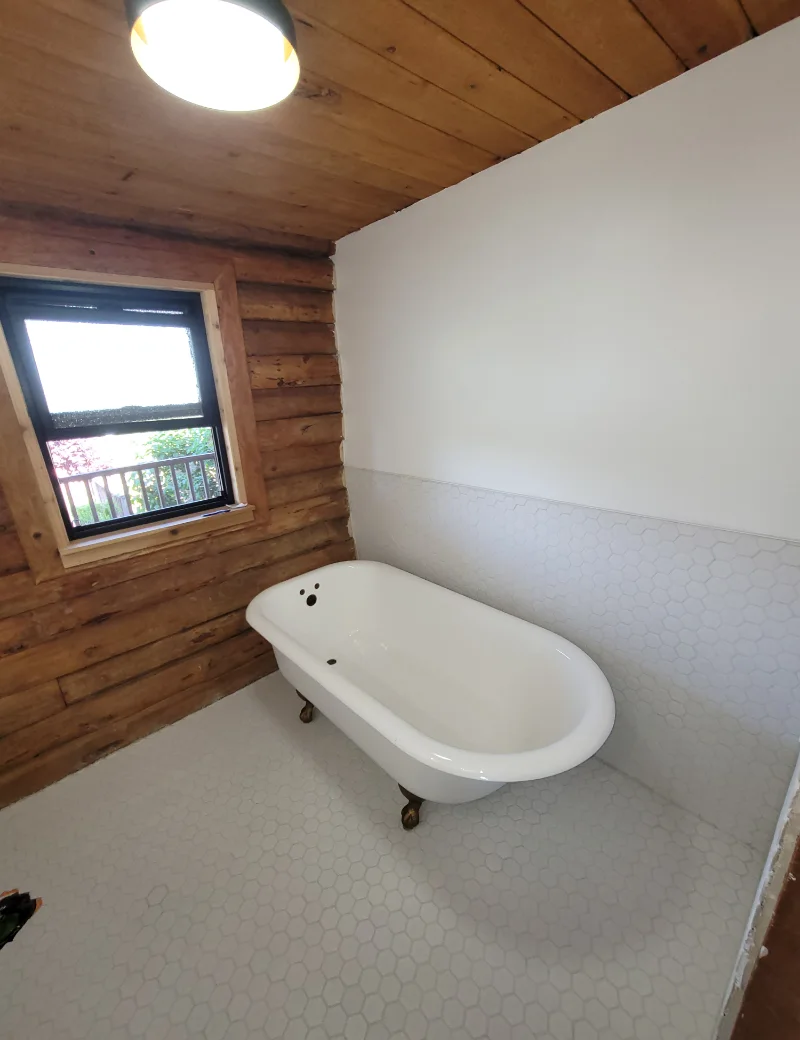 Finished bathroom with clawfoot tub, hexagon tile floor and log wall