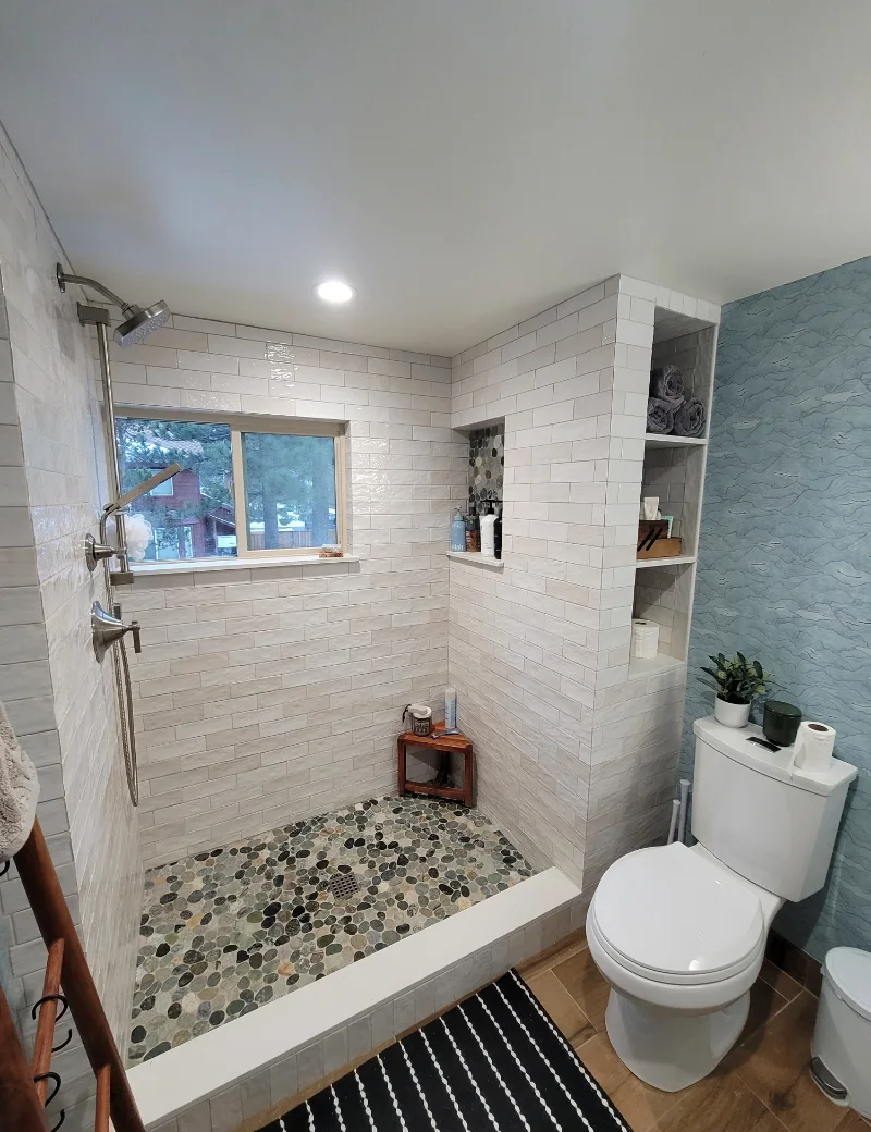 Walk-in shower with white wall tile, pebble floor and built-in shelves