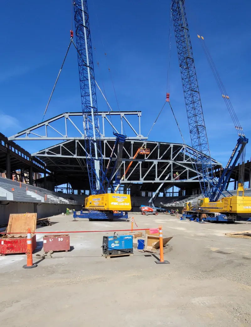 Two cranes lifting a steel roof truss into place